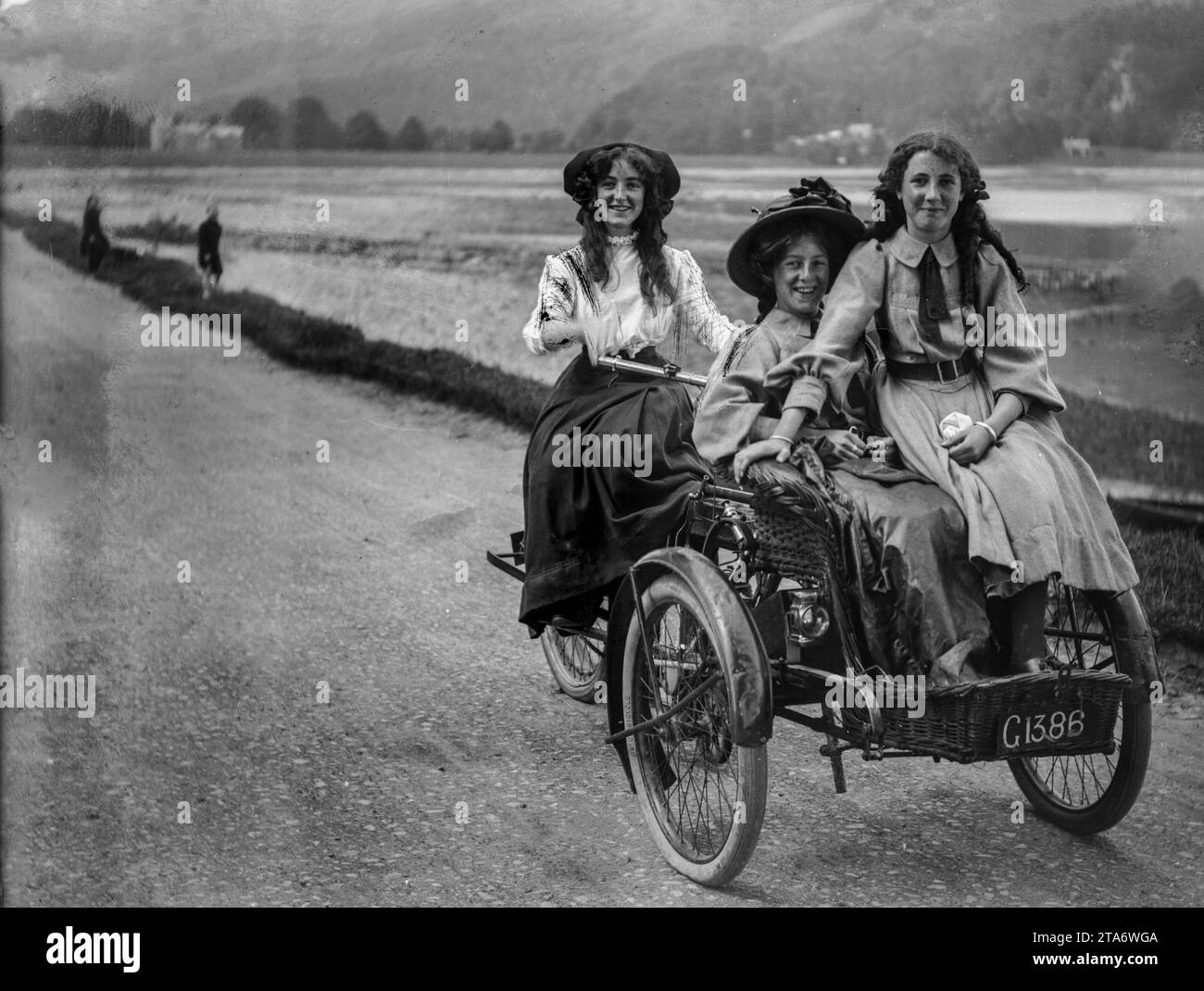 Three Victorian girls from the upper classes ride their tricycle down a country road in the 1890s Stock Photo