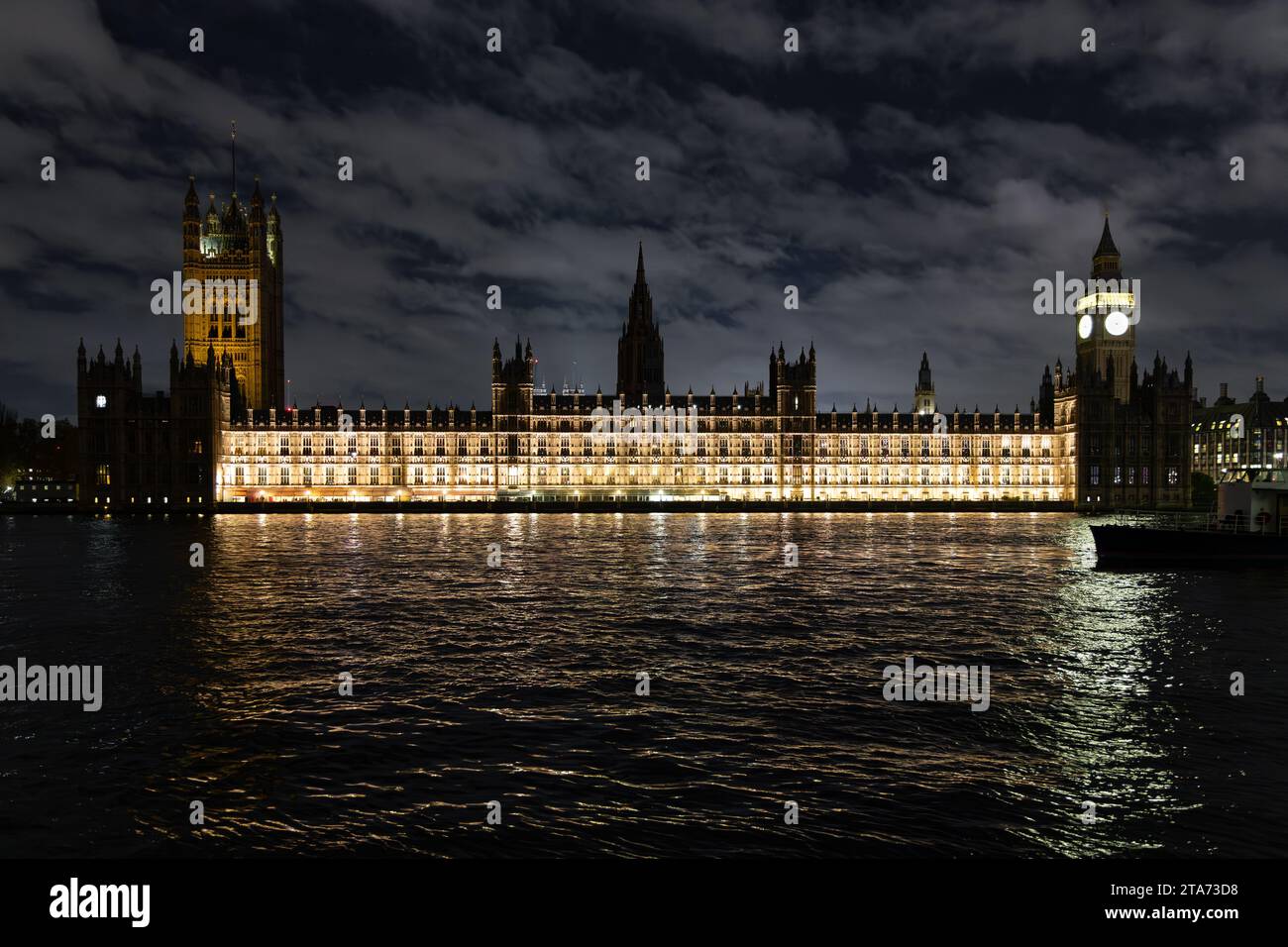 The Palace of Westminster seen lit against a dark sky at night, viewed from the opposite bank of the River Thames, London, UK Stock Photo