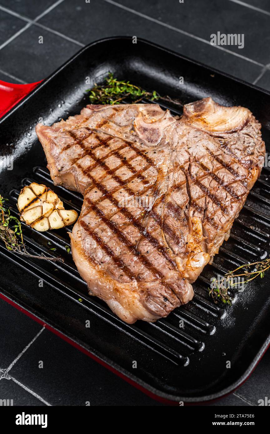 Grilled T-bone, t bone beef meat Steak on a grill skillet. Black background. Top view. Stock Photo