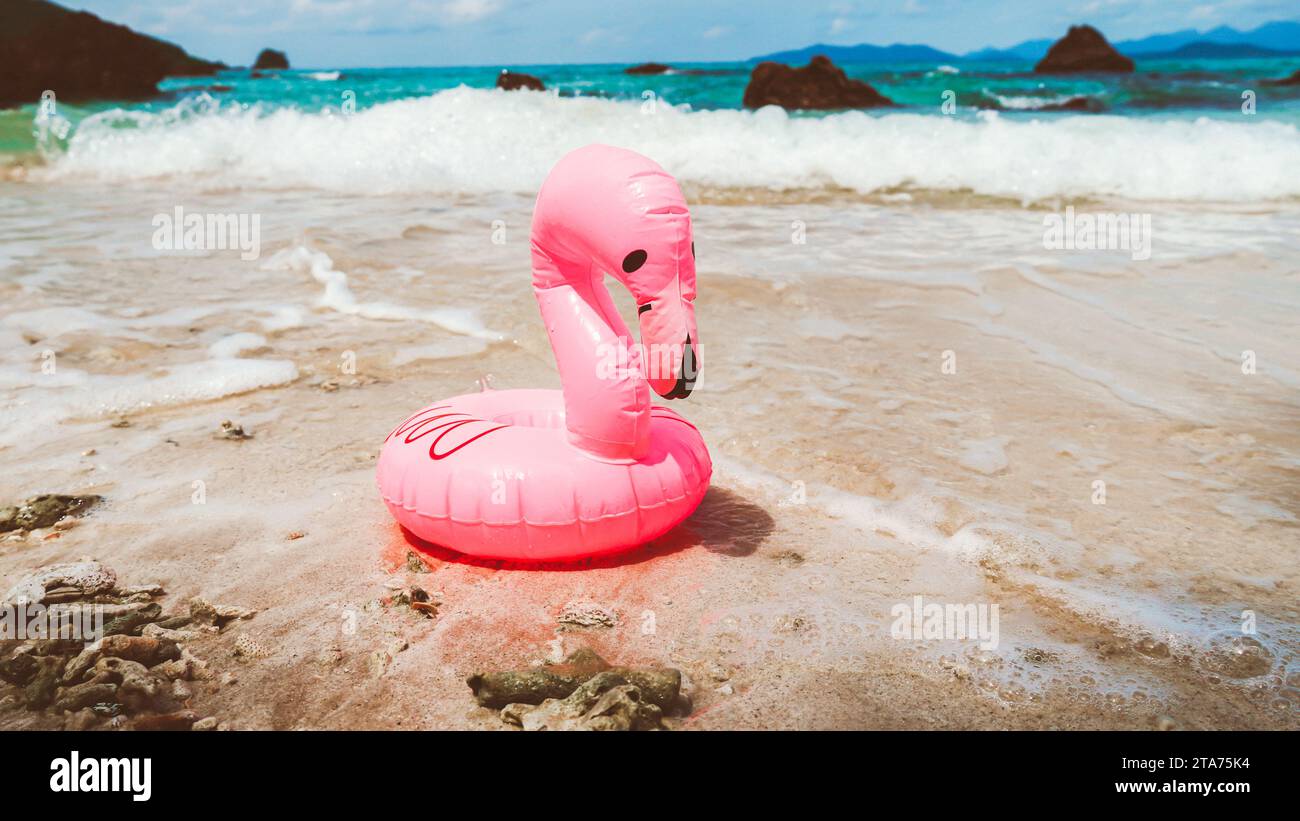 Small Pink rubber life ring on the beach. A swim ring in the shape of a pink flamingo, on the sand of a beach, with the ocean in the background. Stock Photo