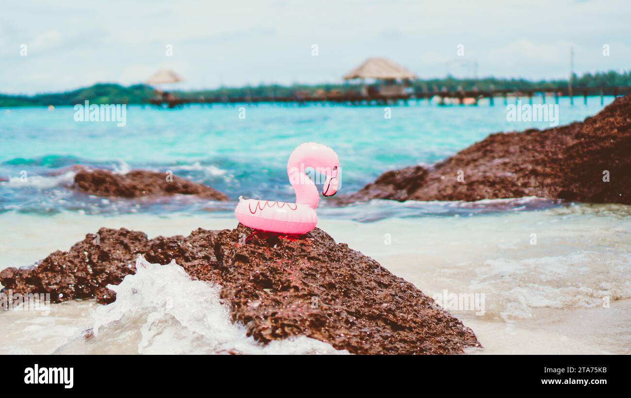 Small Pink rubber life ring on the beach. A swim ring in the shape of a pink flamingo, on the sand of a beach, with the ocean in the background. Stock Photo