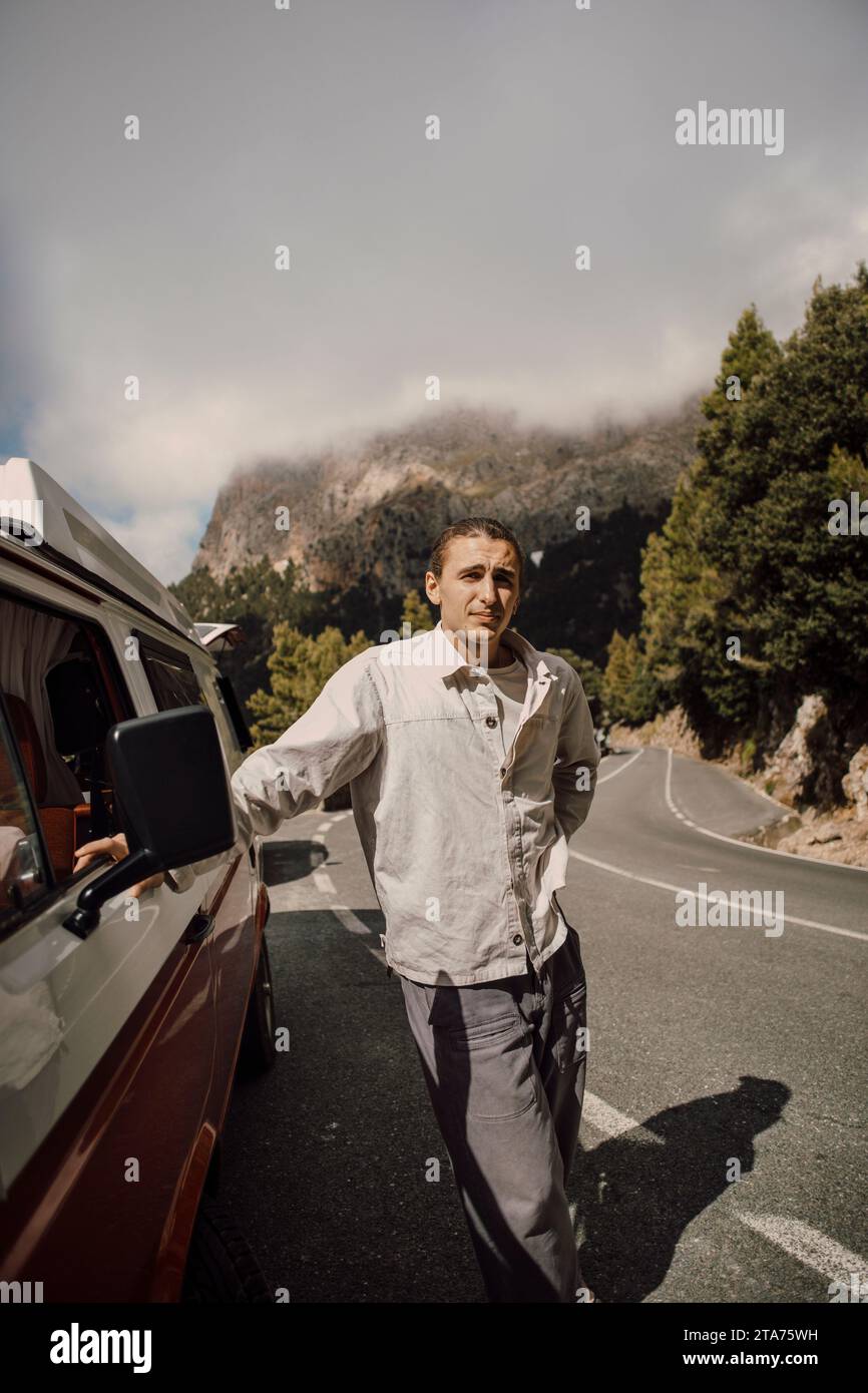Young man leaning on van during road trip Stock Photo