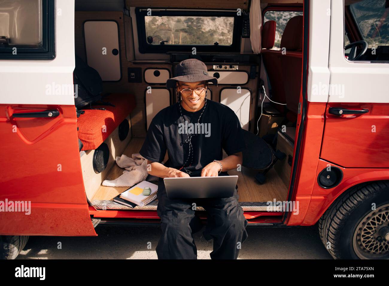 Smiling young man using laptop while sitting in van during road trip Stock Photo