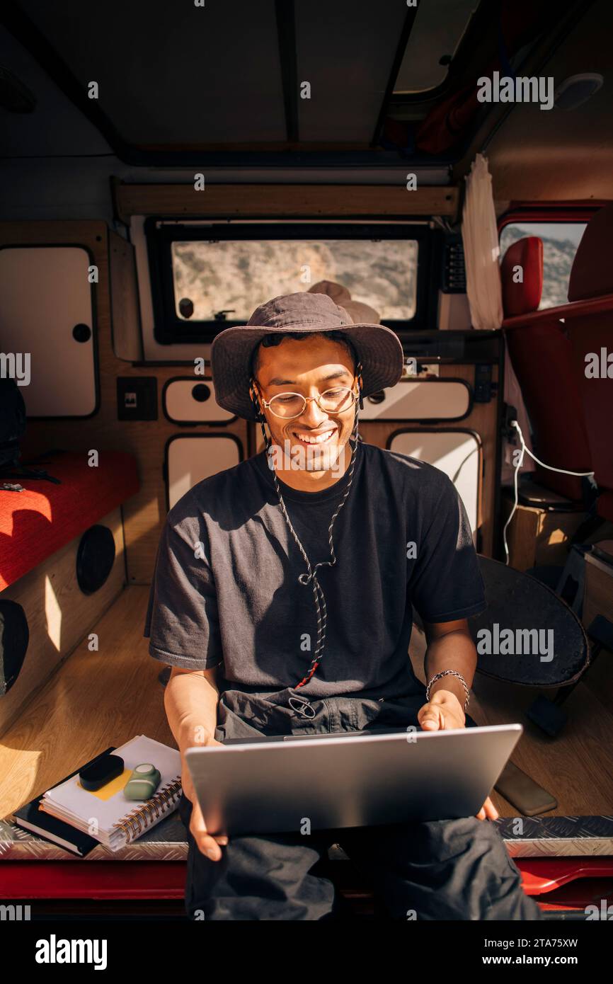 Happy young man using laptop while sitting in van during vacation Stock Photo