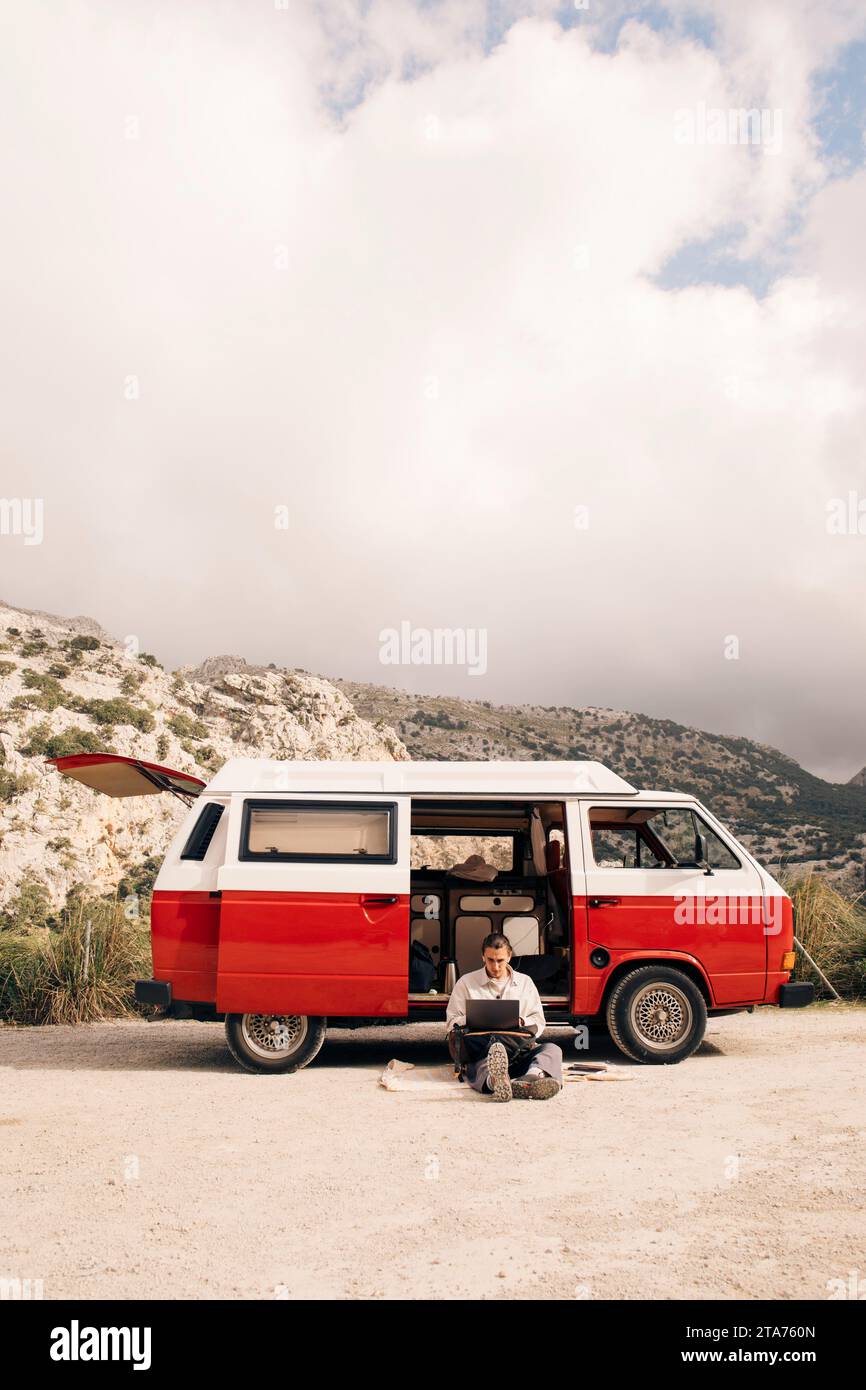 Young man using laptop while sitting near van against sky Stock Photo