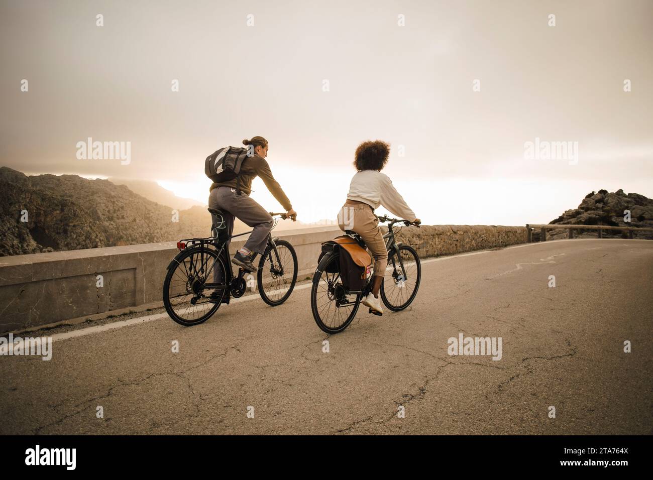 Male and female friends riding bicycles on road against sky Stock Photo