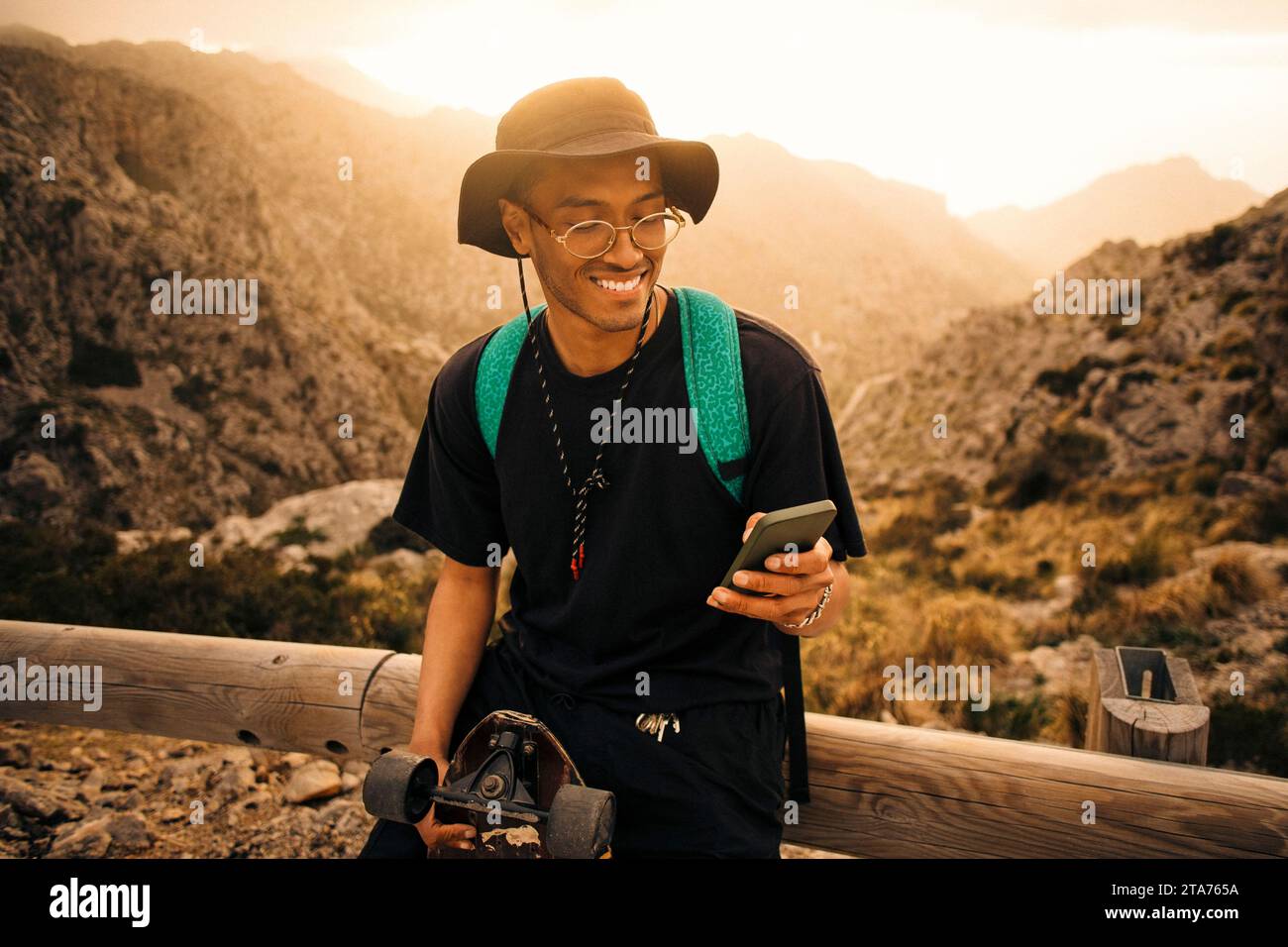 Smiling young man using smart phone while leaning on railing during vacation Stock Photo