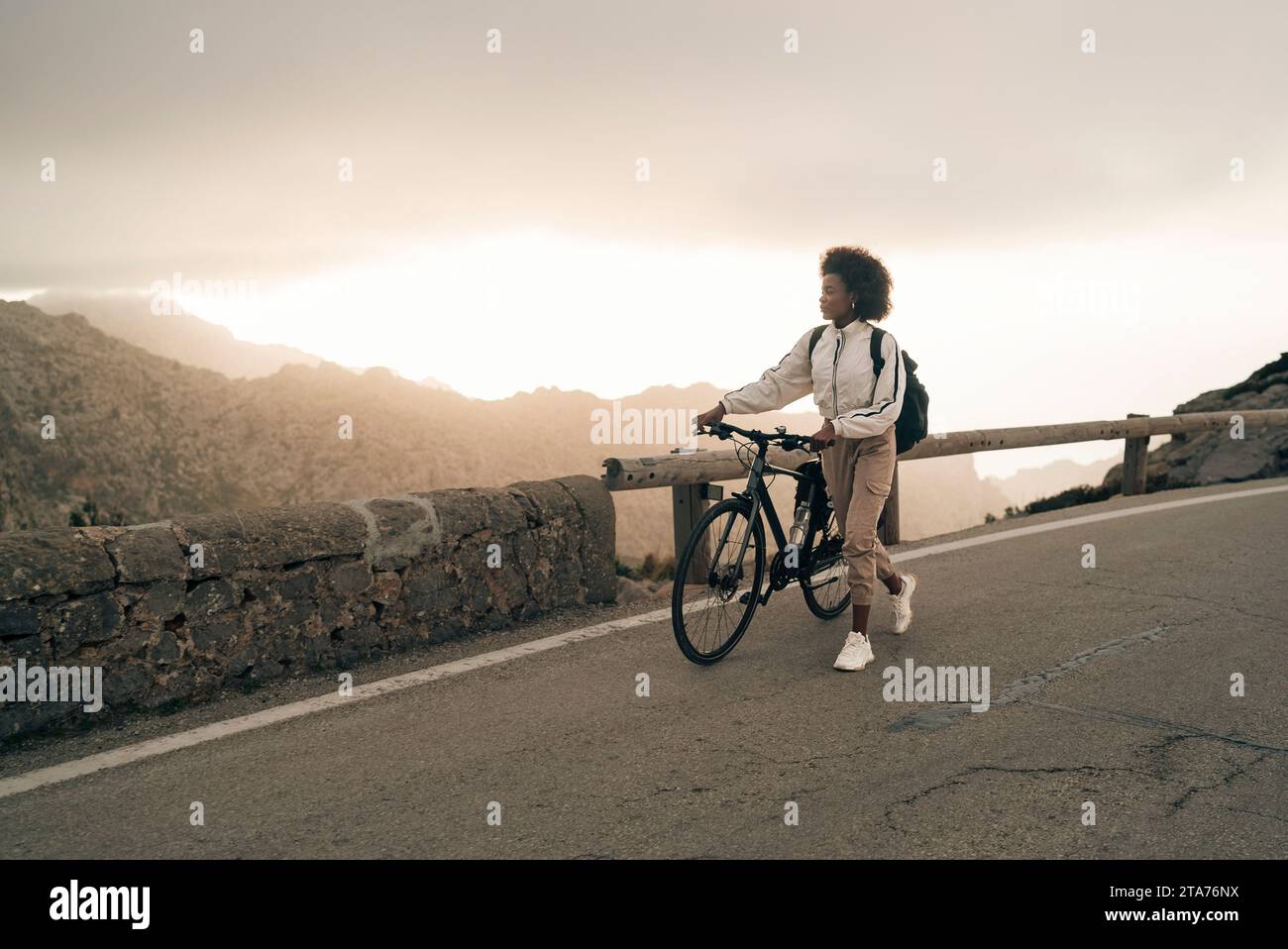 Young woman wheeling cycle on road against sky Stock Photo