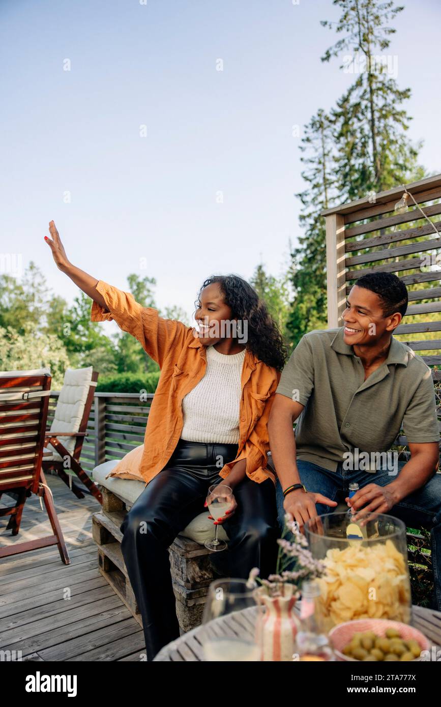 Young woman waving while sitting with male friend during party Stock Photo