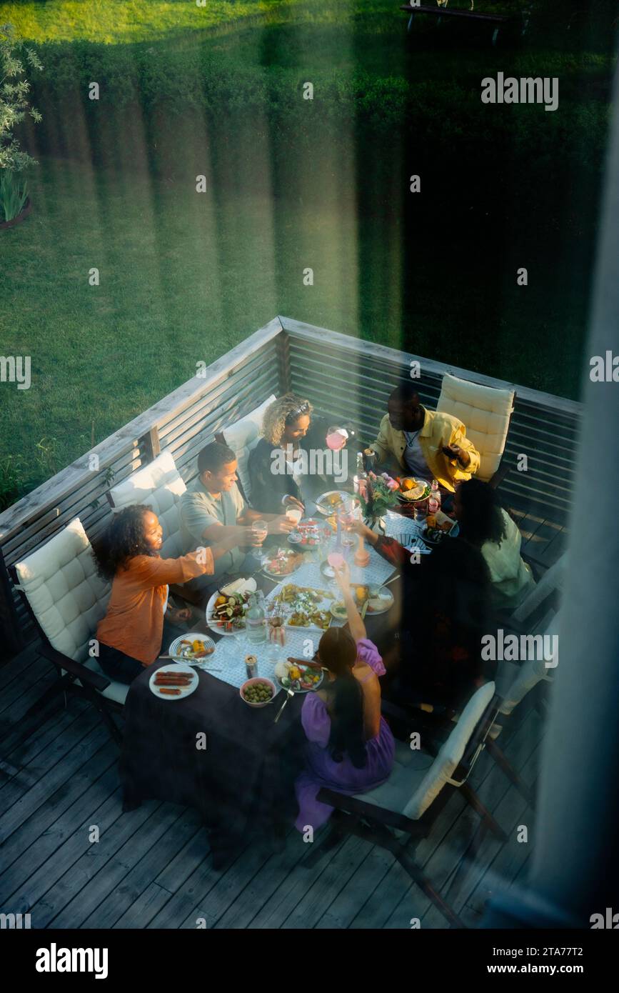 High angle view of male and female friends having food at dining table seen through window Stock Photo