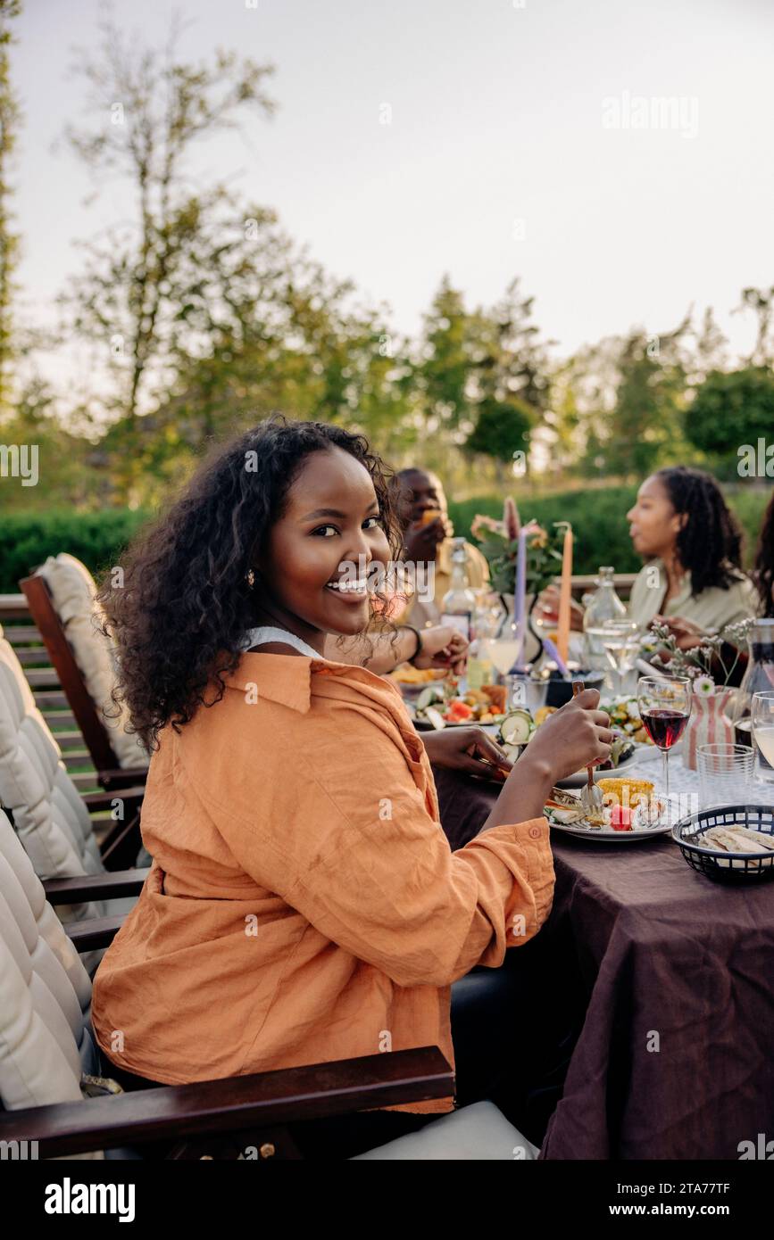 Portrait of smiling woman sitting at dining table during party in back yard Stock Photo