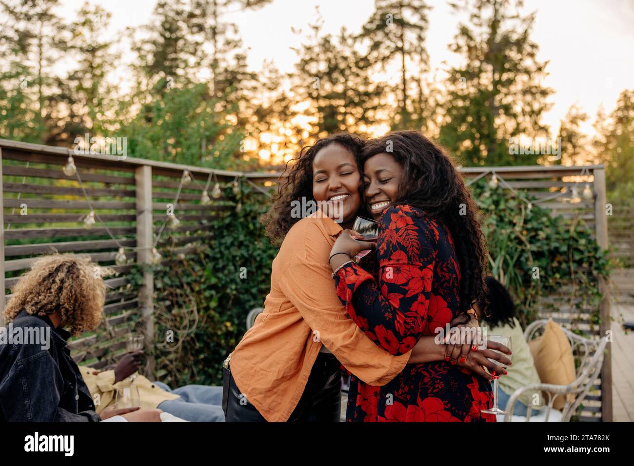 Women with eyes closed embracing each other during dinner party Stock Photo