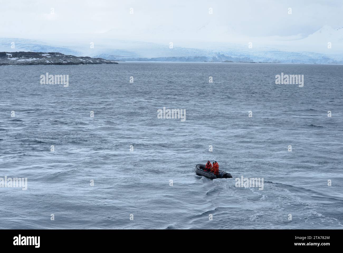 A small rubber boat carrying a team of researchers makes its way through the frigid waters off the coast of Antarctica, with the barren landscape and Stock Photo