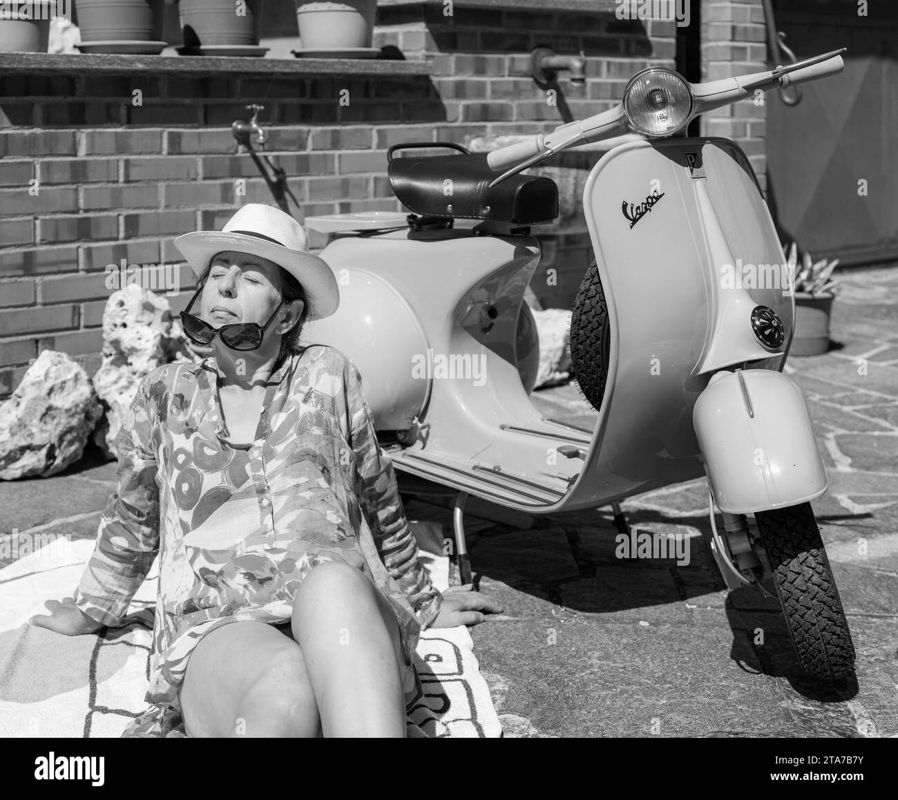 Close-up of a young lady sunbathing next to a 1960s Piaggio Vespa motorcycle Stock Photo