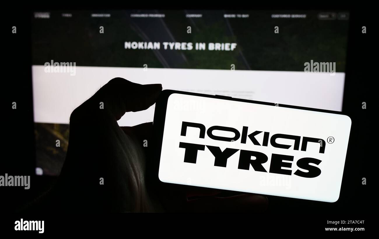 Person holding mobile phone with logo of Finnish tyres manufacturing company Nokian Tyres in front of business web page. Focus on phone display. Stock Photo