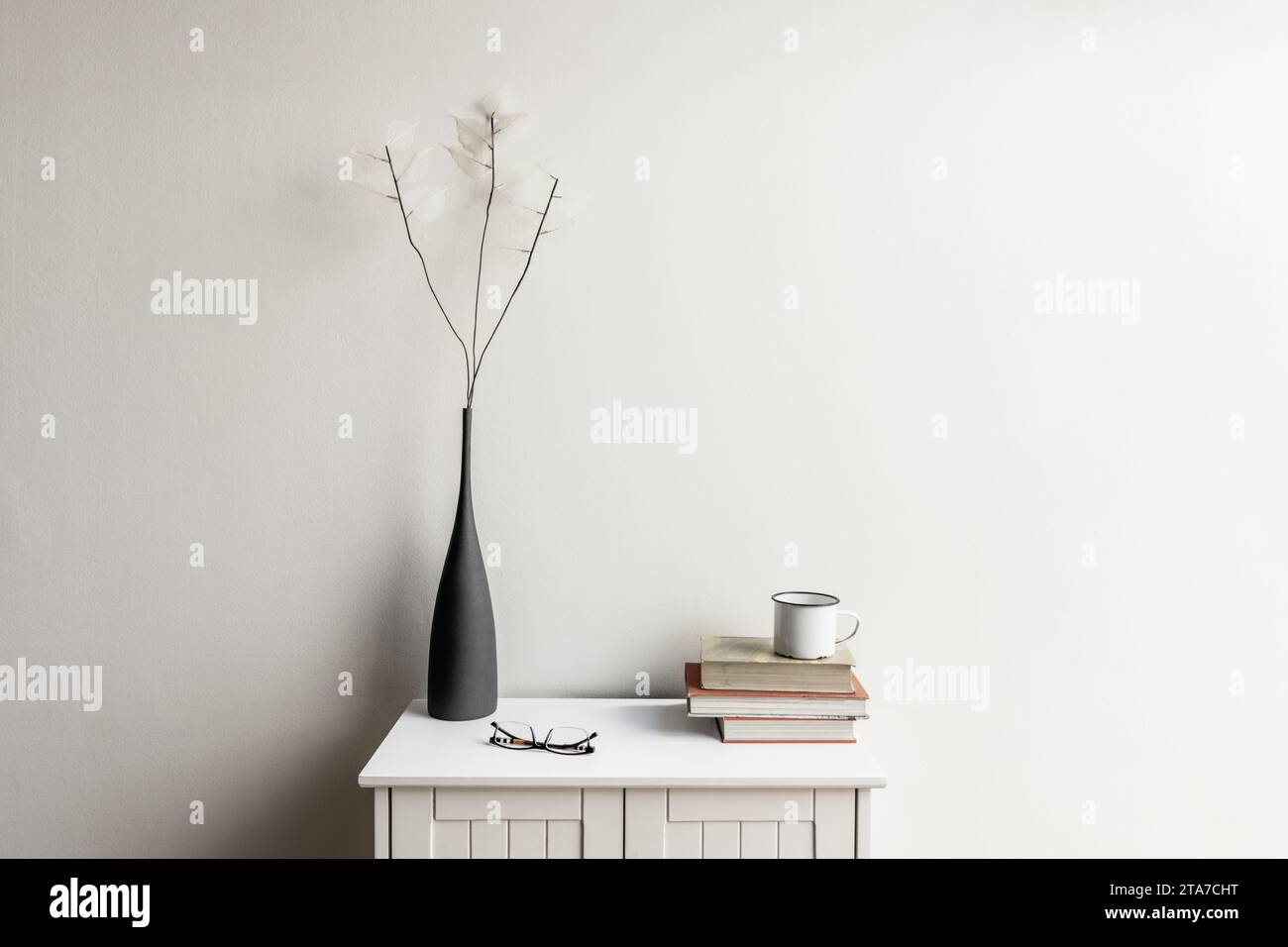 A small white wooden cabinet with a few stacked books Stock Photo