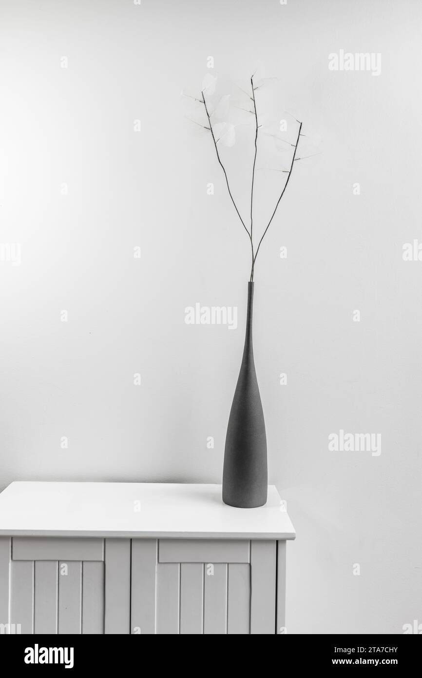 A small white wooden cabinet with a gray vase with artificial branches with subtle white leaves Stock Photo