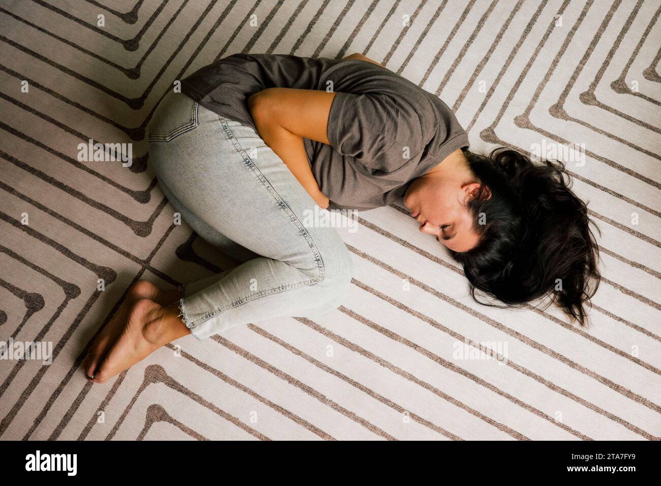 Directly above of lonely woman lying down in fetal position on carpet at home Stock Photo