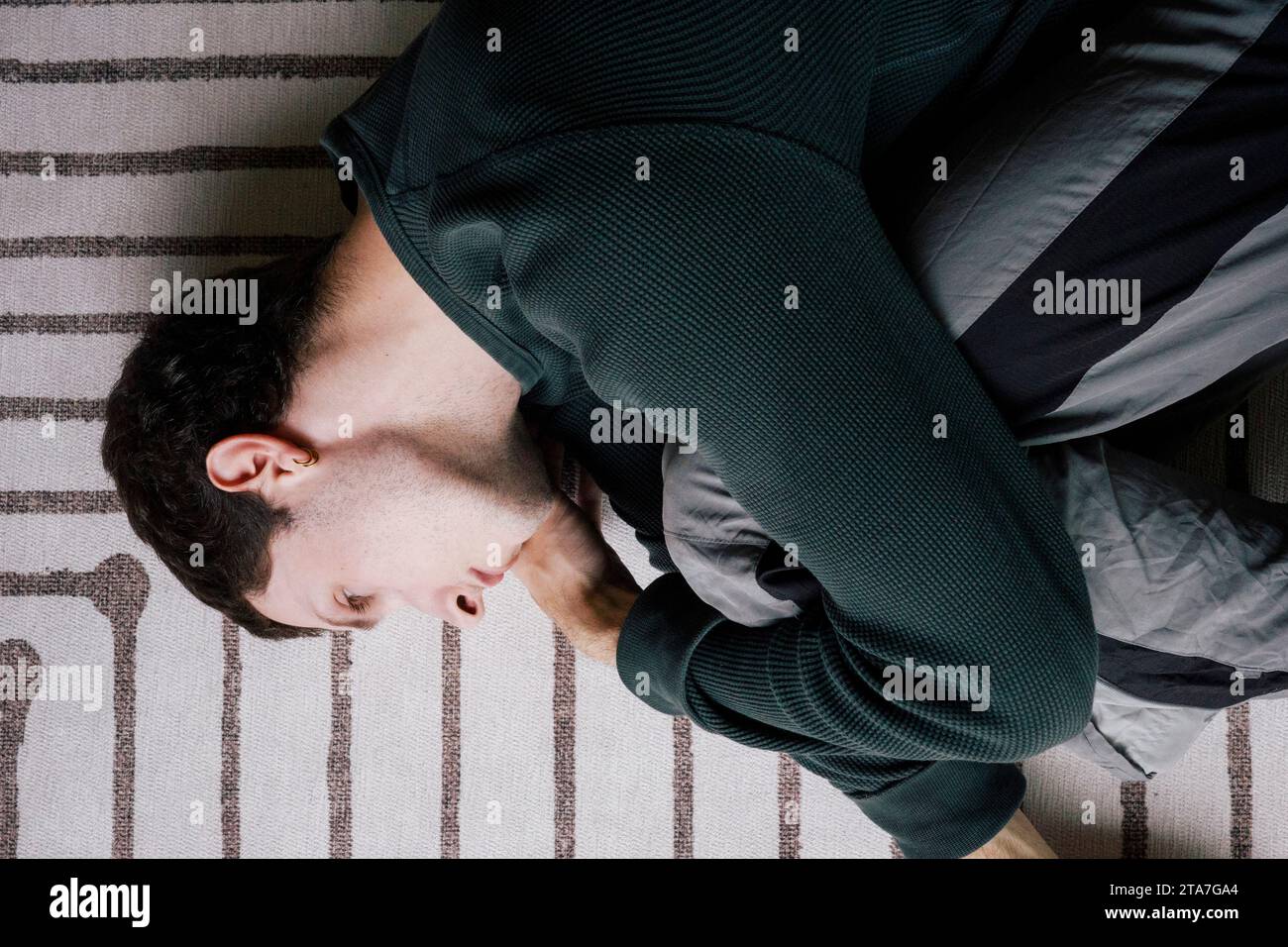 Directly above view of man lying down in fetal position on carpet at home Stock Photo