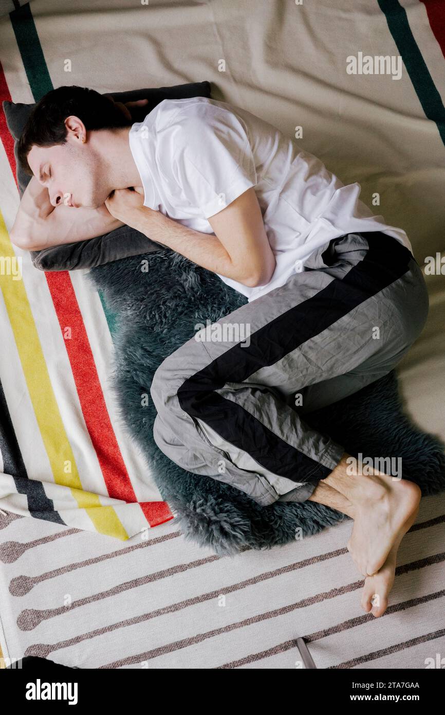 Young depressed man sleeping on carpet at home Stock Photo