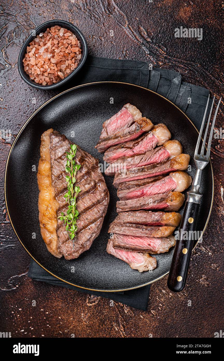 Sliced grilled medium rare Top sirloin beef steak on a plate. Dark background. Top view. Stock Photo