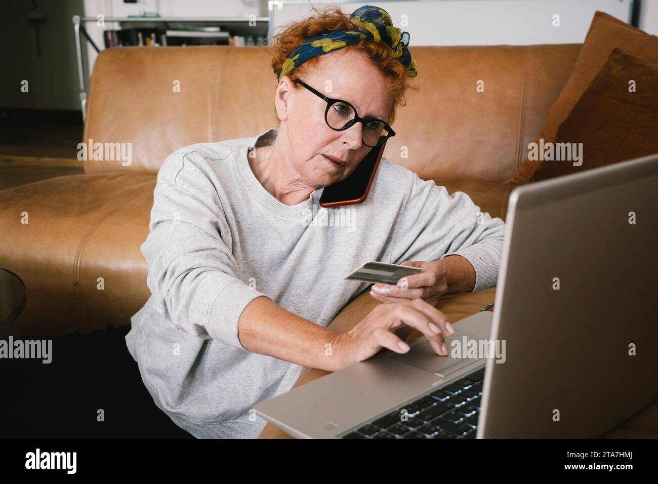 Senior woman talking on smart phone while making online payment through laptop Stock Photo