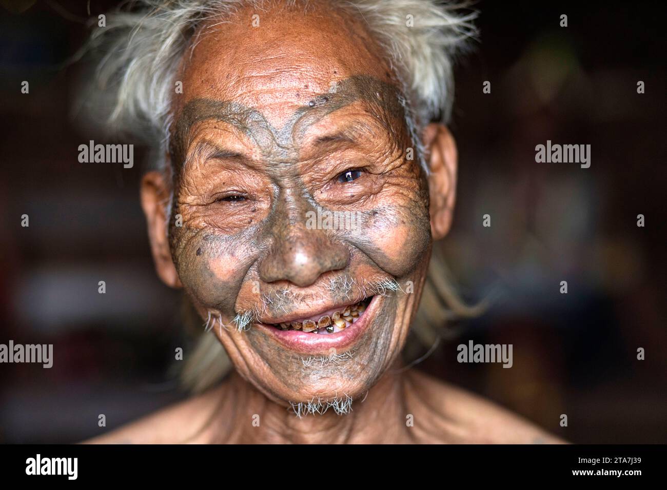Portarit of an elder, a man from a konyak tribe with traditional tribal tattoos on his face , smiling in the camera, Nagaland, India Stock Photo