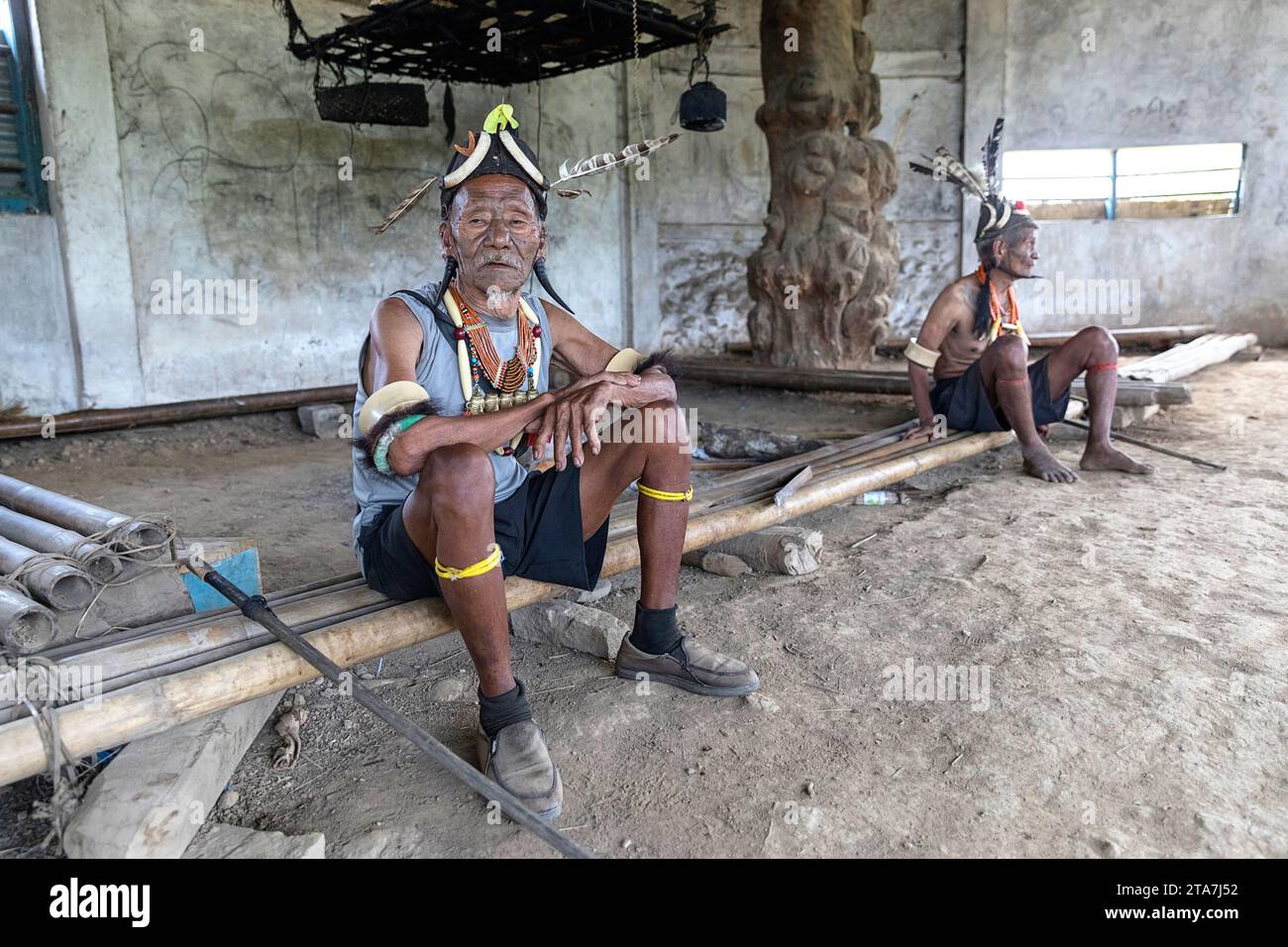 Konyak elders, warriors dressed in spectacular traditional costume in a traditional men longhouse in a small villlage near Mon in Nagaland, India Stock Photo