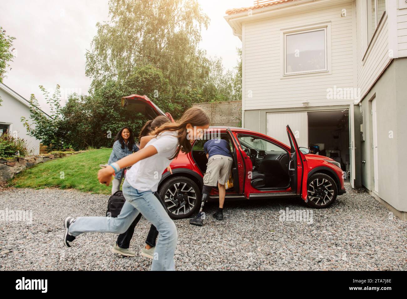 Cheerful daughters playing near electric car by house Stock Photo