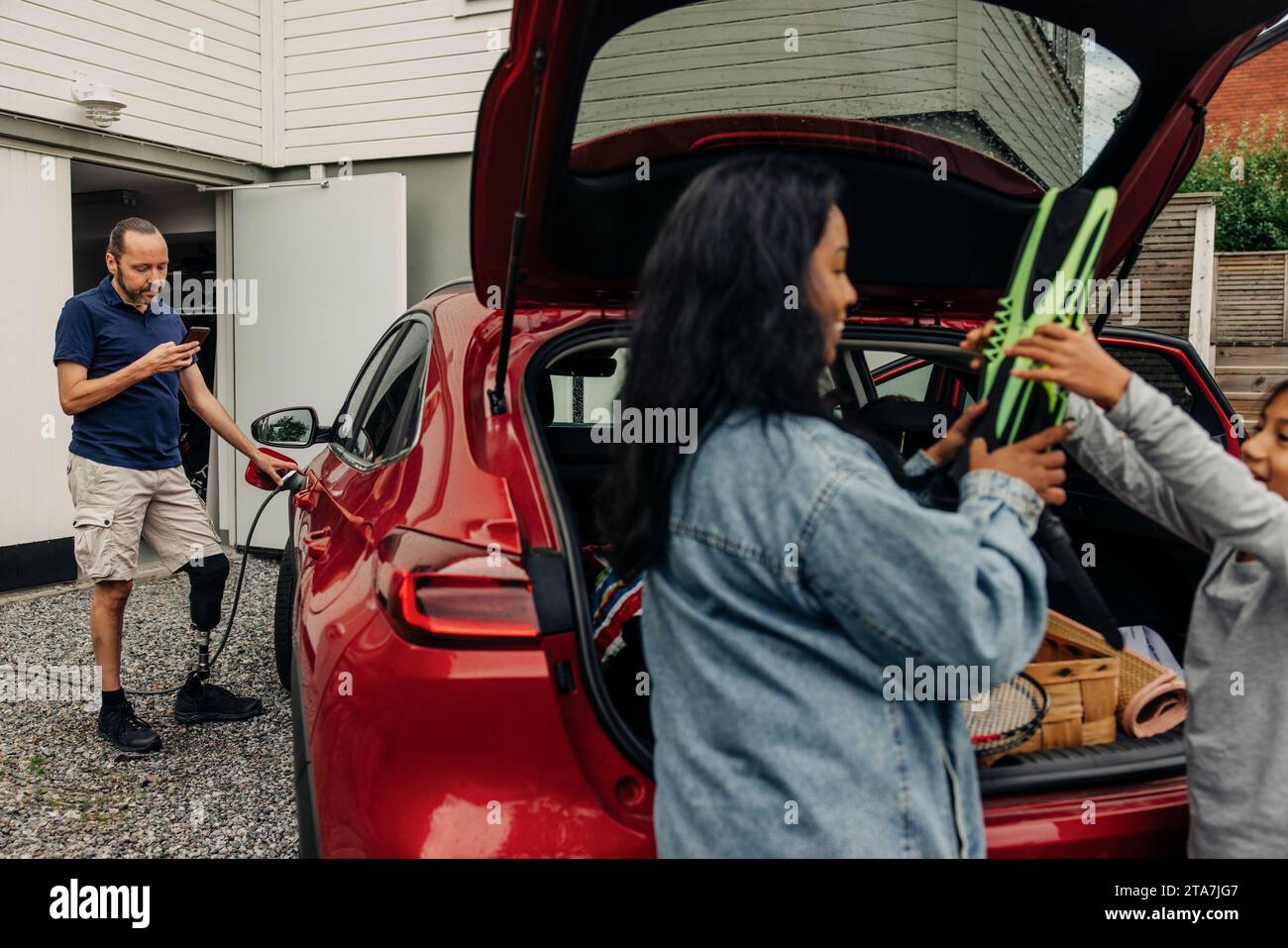 Man with disability using smart phone while charging electric car Stock Photo