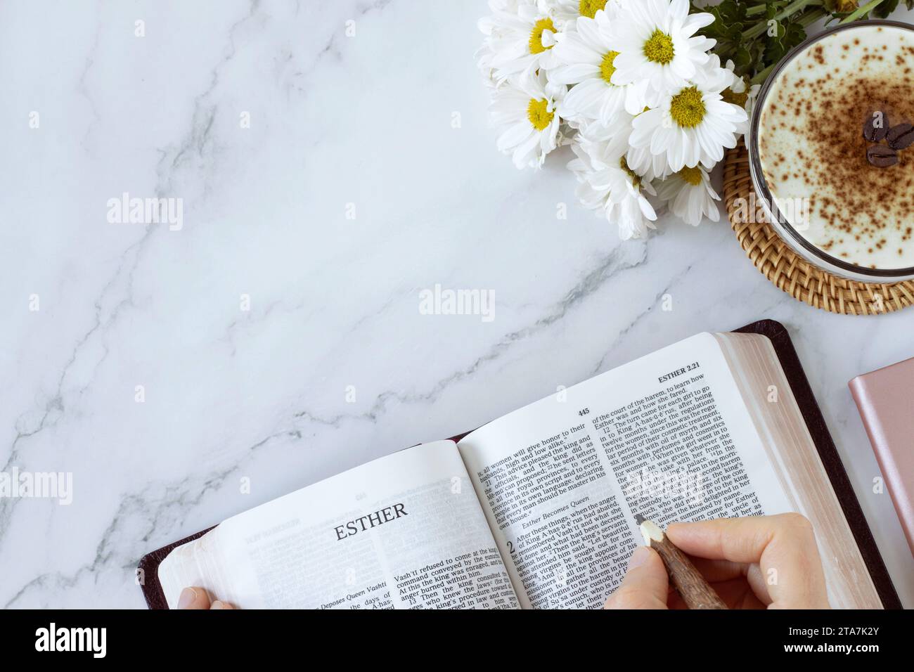 Open holy bible book of Esther with cup of coffee and flowers on white marble background. Top view, copy space. Studying Old Testament Scriptures. Stock Photo