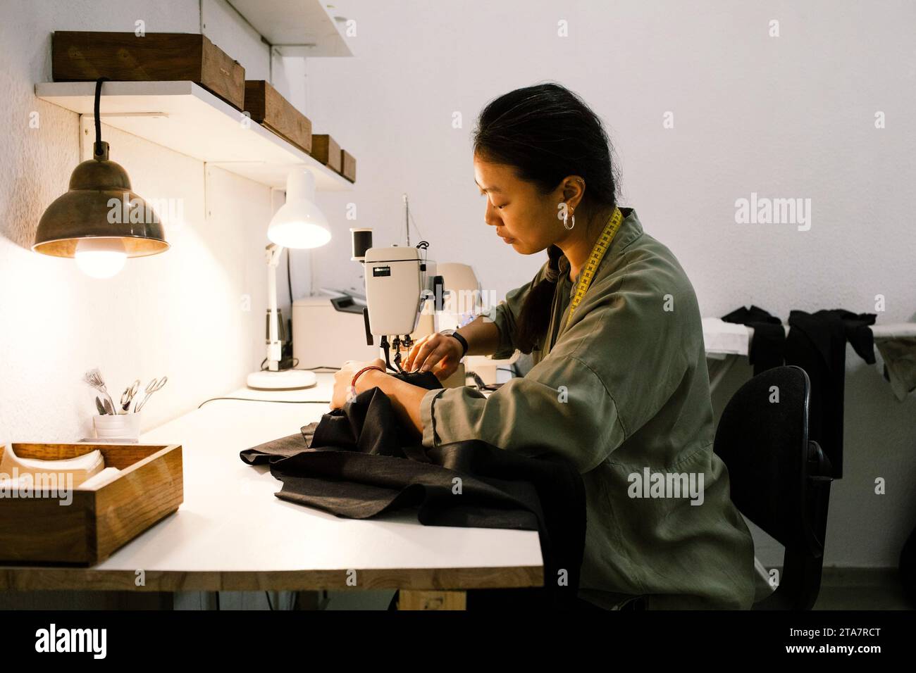 Side view of young seamstress making dress using sewing machine while