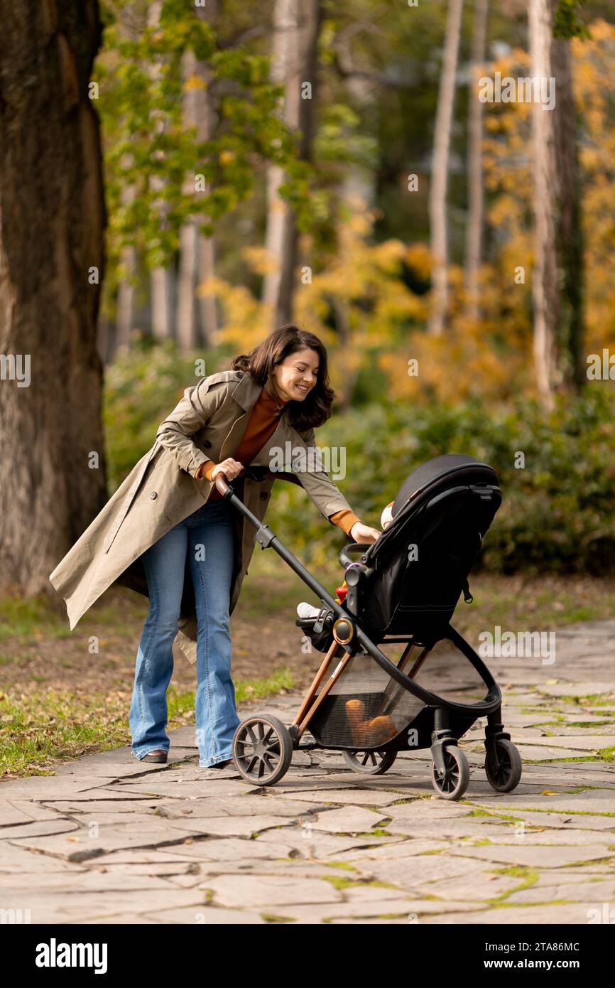Young woman with a cute baby girl in baby stroller at the autumn park Stock Photo