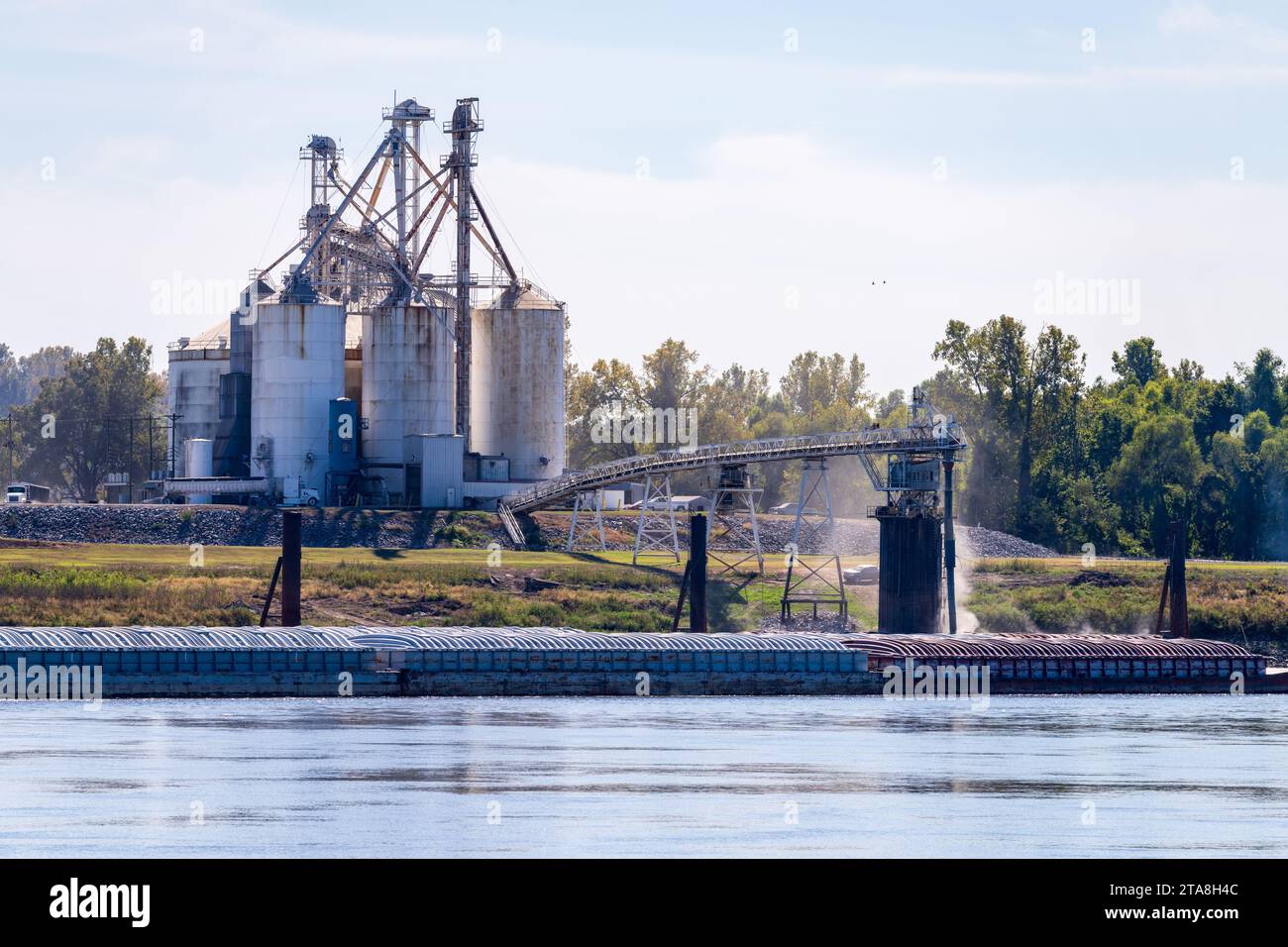 Tugboat pushing freight barges past grain loading dock in farming