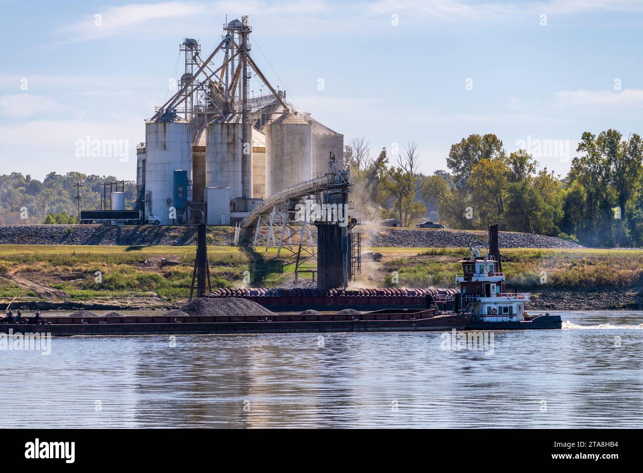 Tugboat pushing freight barges past grain loading dock in farming