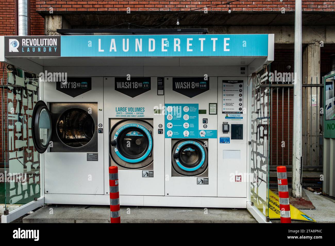 Automated self-service launderette with industrial washing and drying machines in urban setting. Stock Photo