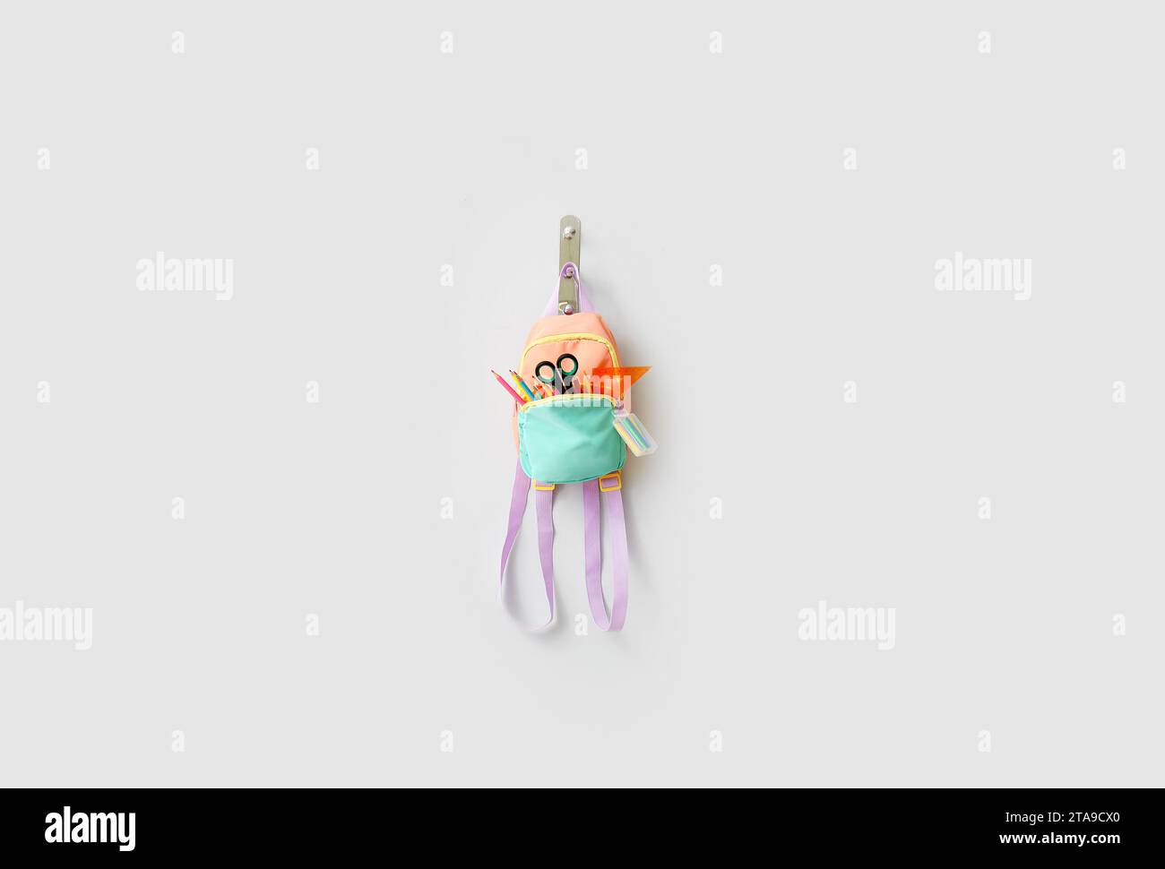 Stylish backpack with different stationery hanging on light wall Stock Photo