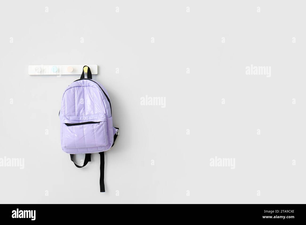 School backpack hanging on light wall Stock Photo