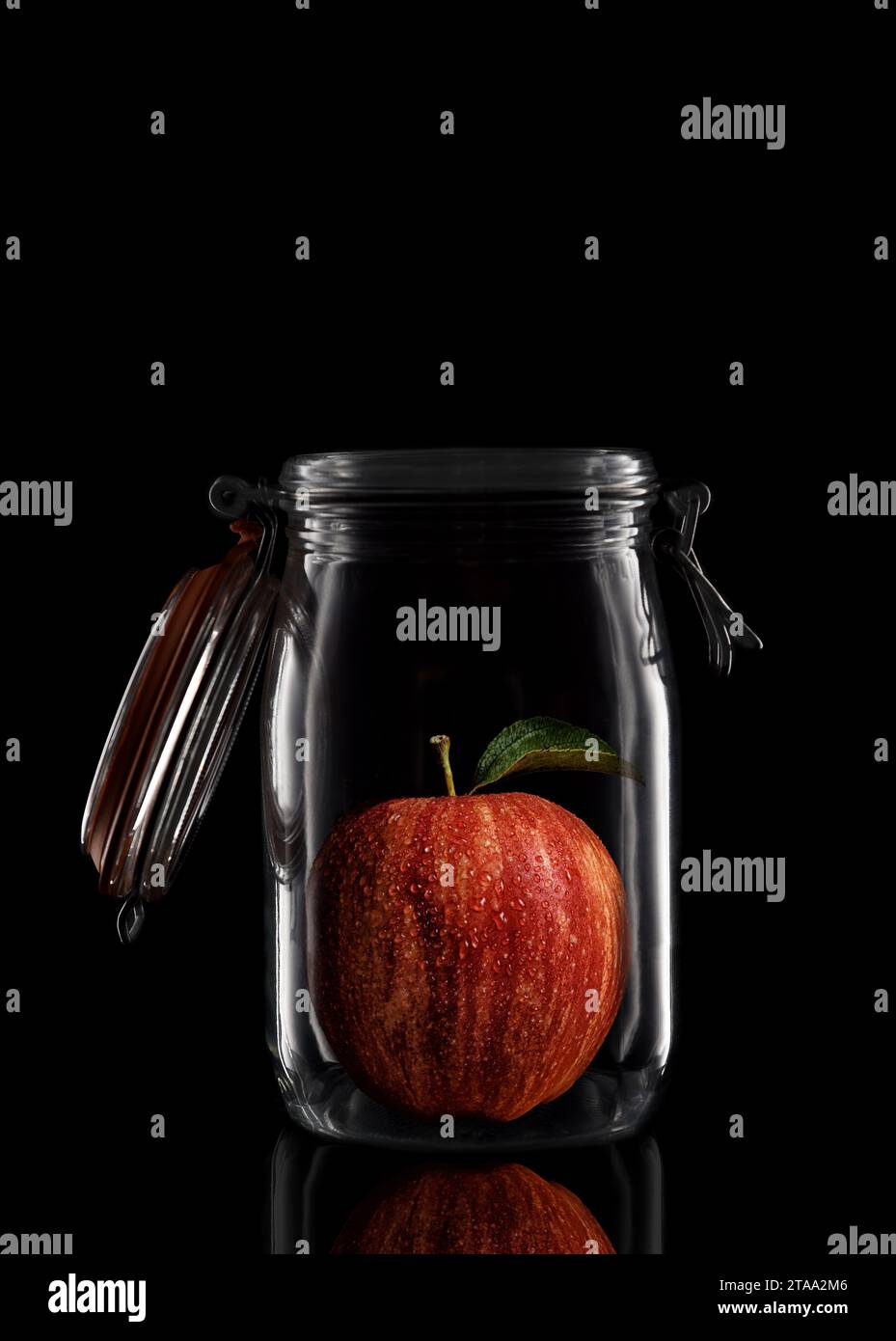 A Gala Apple inside a glass storage or canning jar isolated on black with reflection, with lid open. Stock Photo