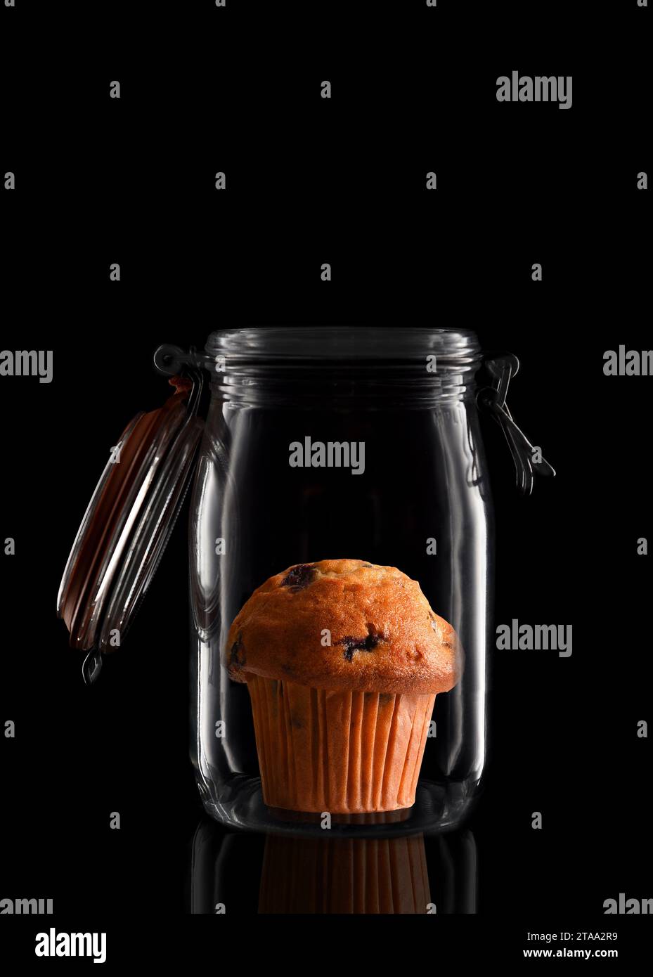 A Blueberry Muffin in a glass storage or canning jar isolated on black with reflection, with lid open. Stock Photo