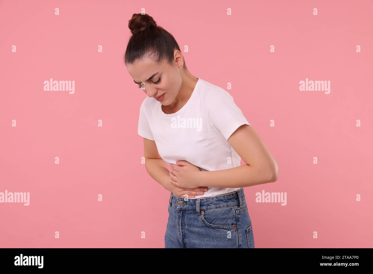 Woman suffering from abdominal pain on pink background. Unhealthy