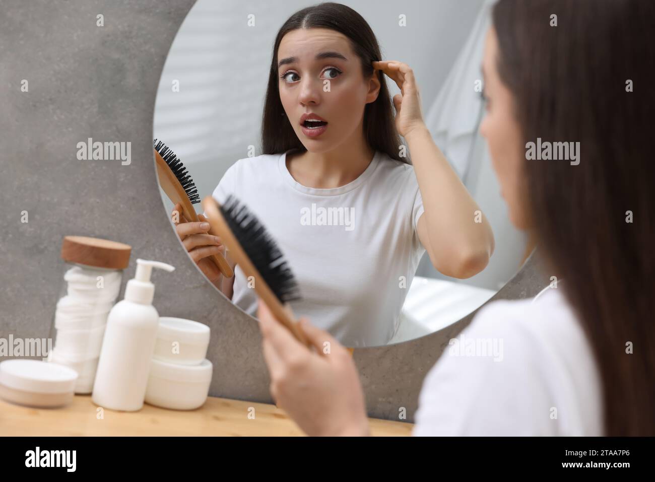 Emotional woman with brush suffering from dandruff near mirror at home. Stock Photo