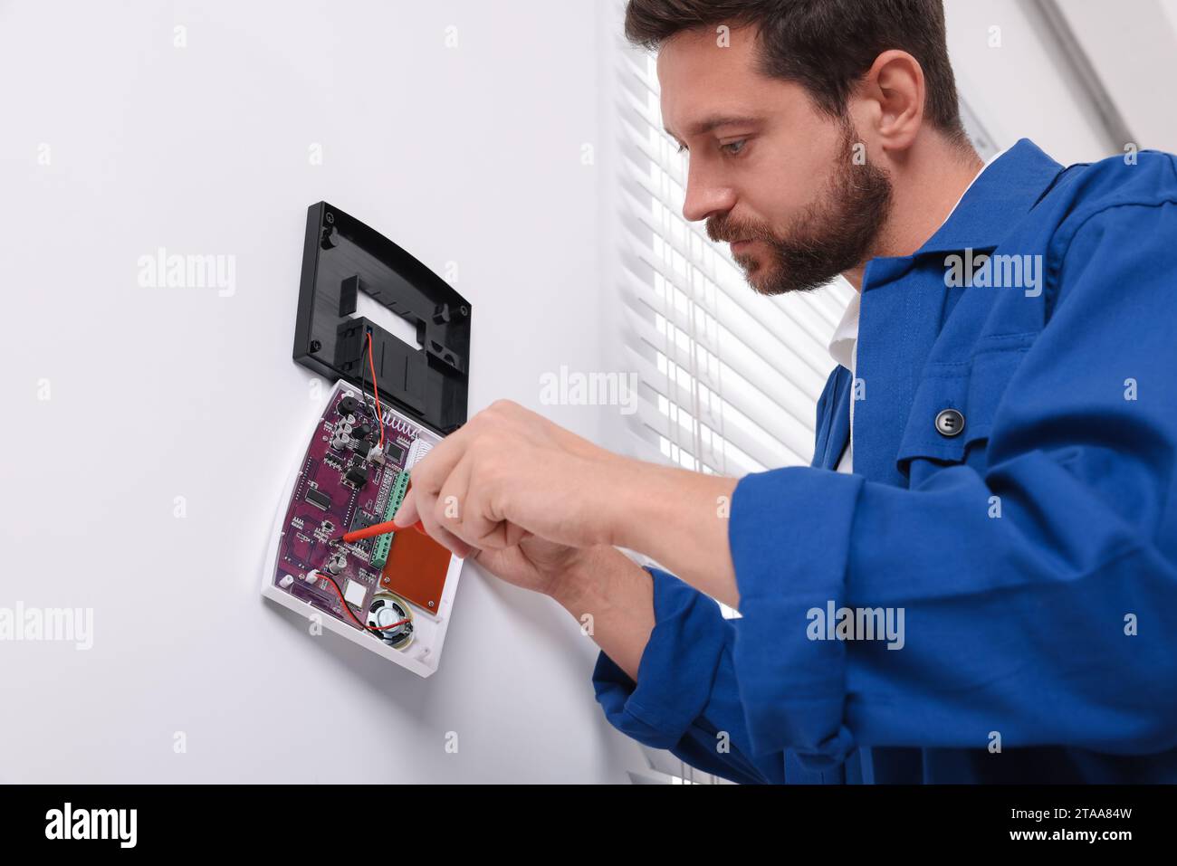 Technician installing home security alarm system on white wall indoors Stock Photo