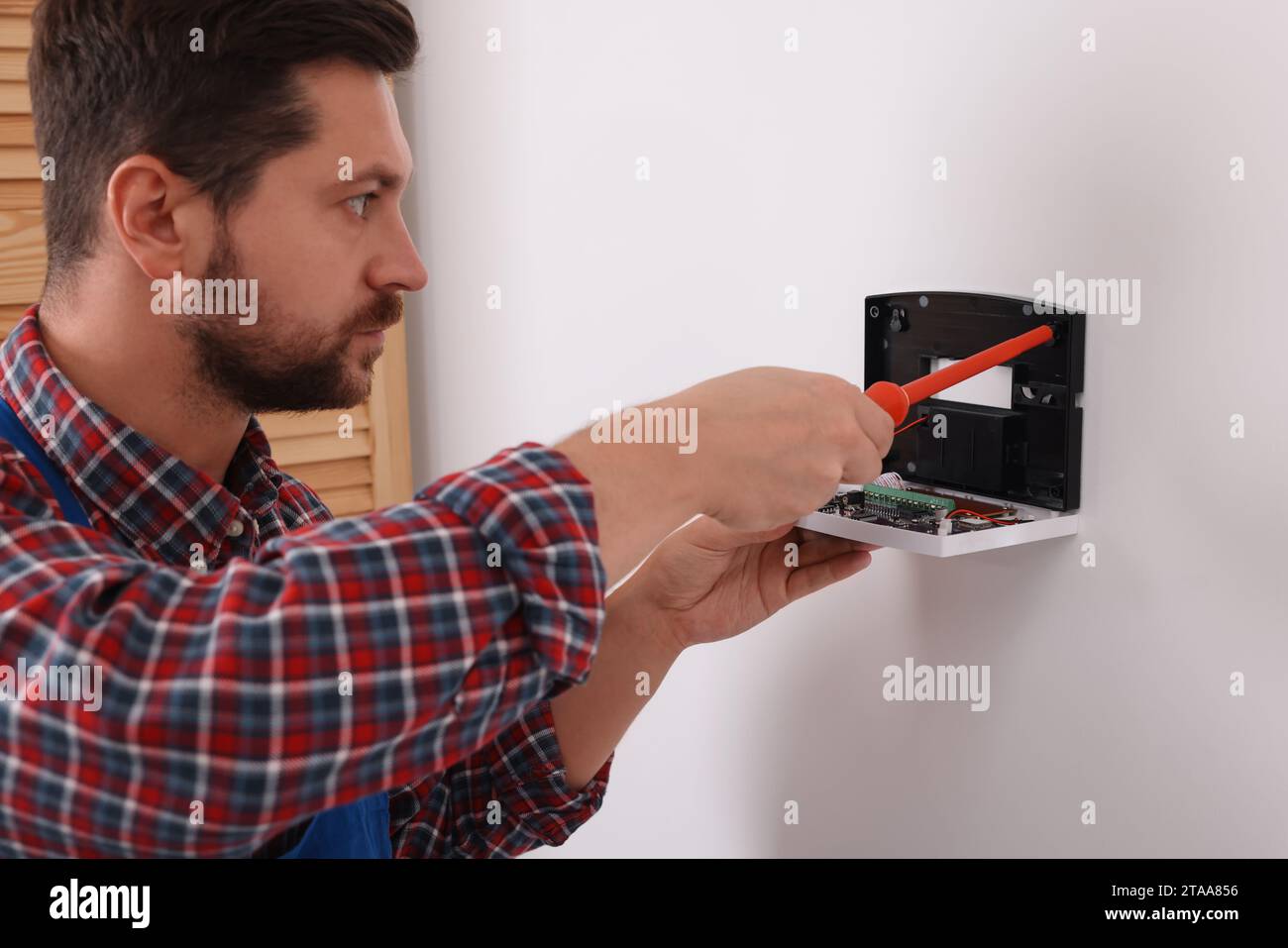 Technician installing home security alarm system on white wall indoors Stock Photo