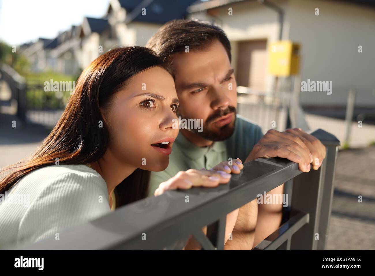 Concept of private life. Curious couple spying on neighbours over fence outdoors Stock Photo