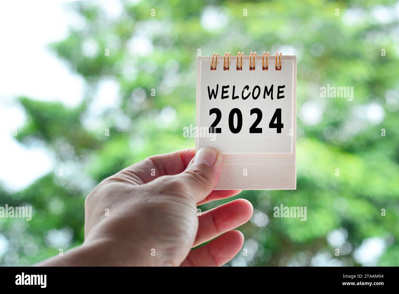 Hands Holding Calendar 2024 with blurred green background. Happy New