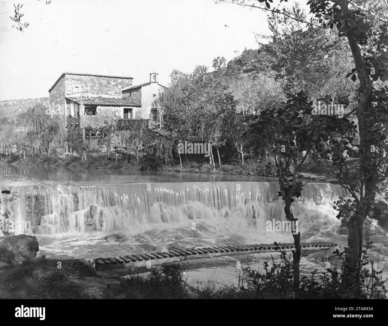 Vista general de la rectoria de Santa Eugènia, en primer pla una petita presa i una passera al riu. Stock Photo