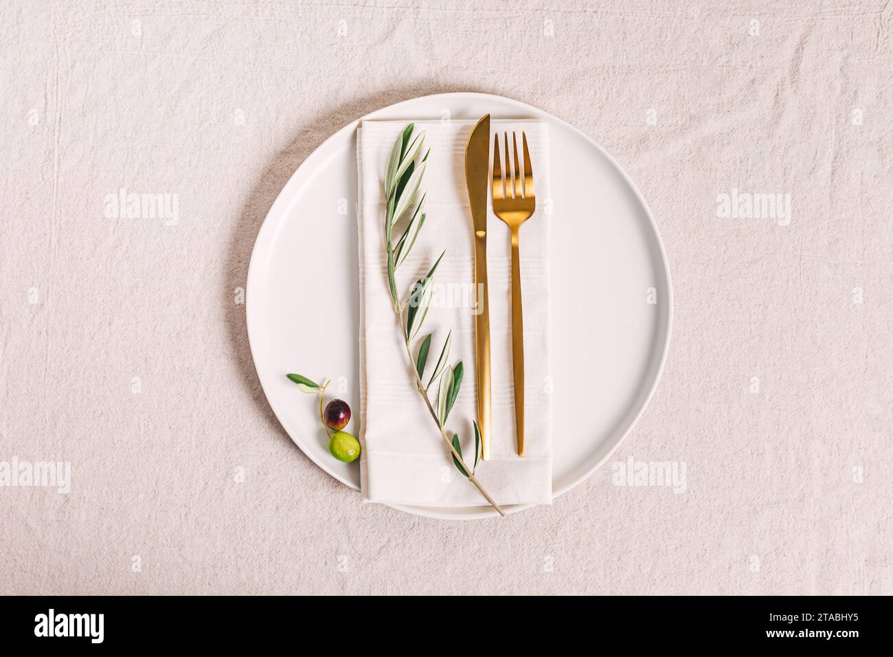 Plate with golden color cutlery and olive branch, elegant table setting ...