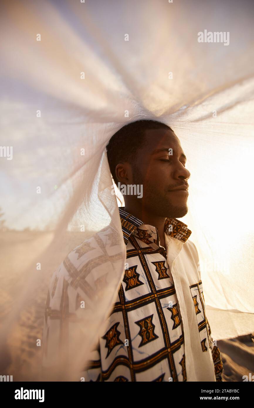 Vertical portrait of African American man wearing traditional clothing looking away outdoors covered with veil Stock Photo