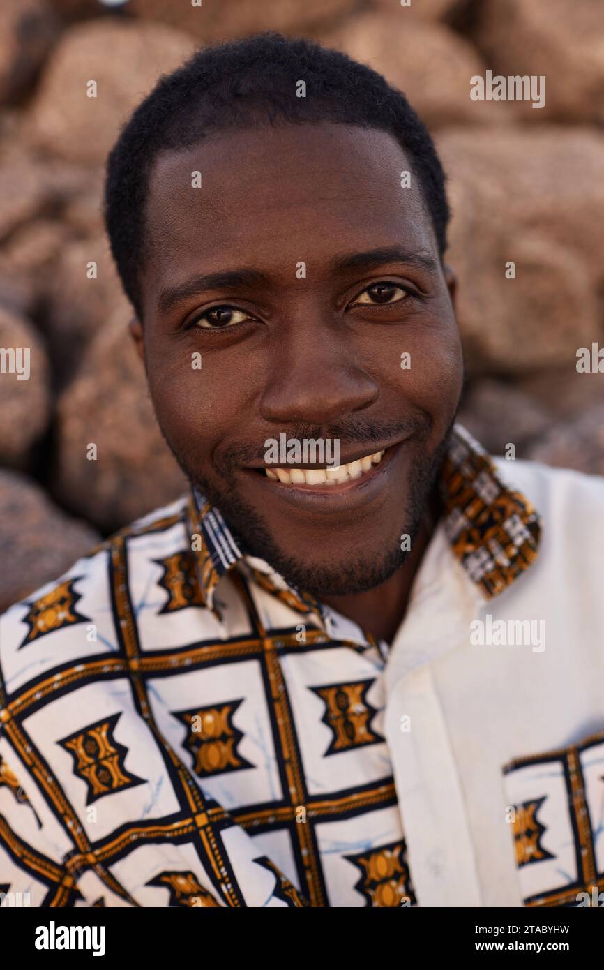 Vertical closeup portrait of smiling African American man wearing traditional print and looking at camera outdoors Stock Photo
